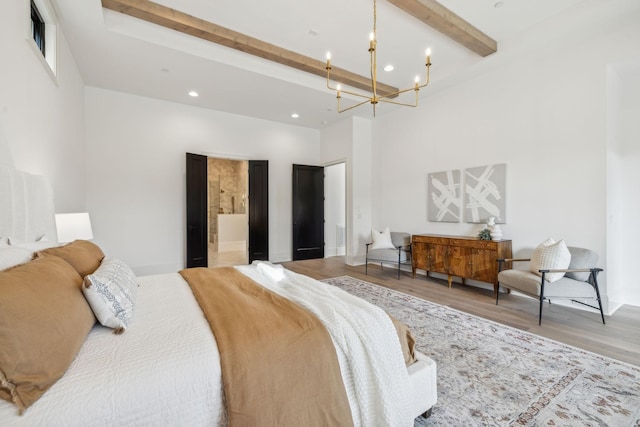 bedroom with beam ceiling, ensuite bath, a notable chandelier, a towering ceiling, and hardwood / wood-style flooring