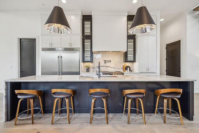 kitchen with light hardwood / wood-style floors, tasteful backsplash, a large island with sink, and built in refrigerator