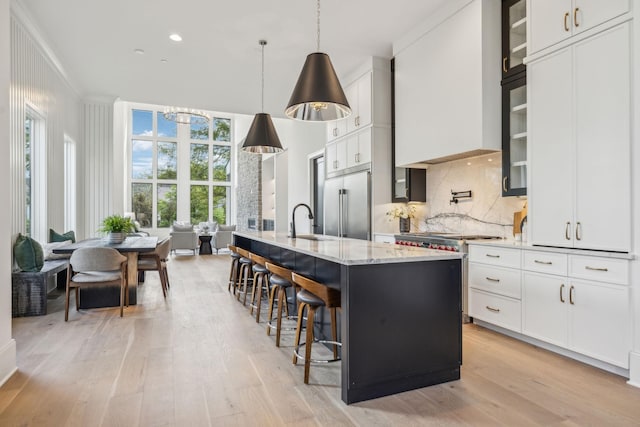 kitchen featuring pendant lighting, backsplash, a kitchen island with sink, stainless steel built in fridge, and white cabinetry