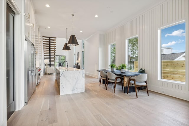 kitchen featuring a kitchen island with sink, white cabinets, sink, hanging light fixtures, and light stone counters