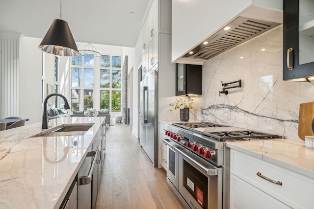 kitchen with light stone countertops, premium appliances, white cabinetry, and sink