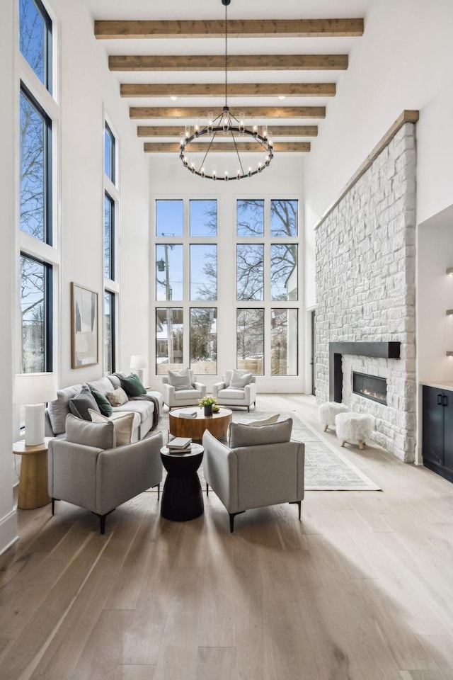 living room with a chandelier, beam ceiling, a stone fireplace, and wood-type flooring