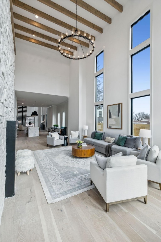 living room featuring beam ceiling, light hardwood / wood-style floors, a high ceiling, and an inviting chandelier