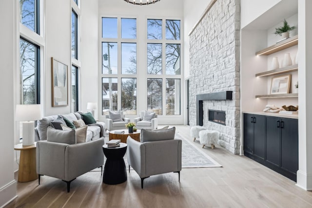 living room featuring light wood-type flooring, a towering ceiling, and a stone fireplace