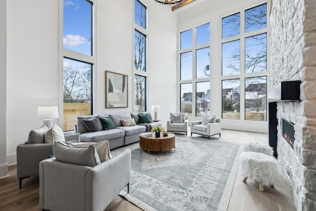 living room featuring hardwood / wood-style floors, a towering ceiling, a stone fireplace, and plenty of natural light