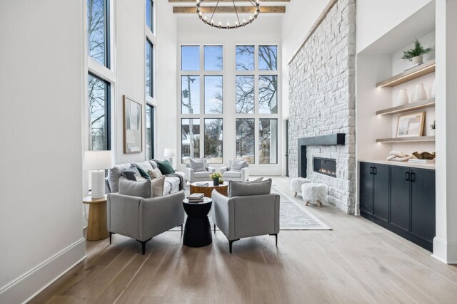 living room featuring a high ceiling, an inviting chandelier, light hardwood / wood-style flooring, and a stone fireplace