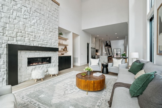 living room with a high ceiling, light wood-type flooring, and a stone fireplace