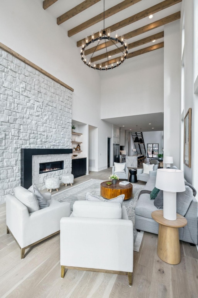 living room featuring beamed ceiling, a notable chandelier, a towering ceiling, light hardwood / wood-style floors, and a fireplace