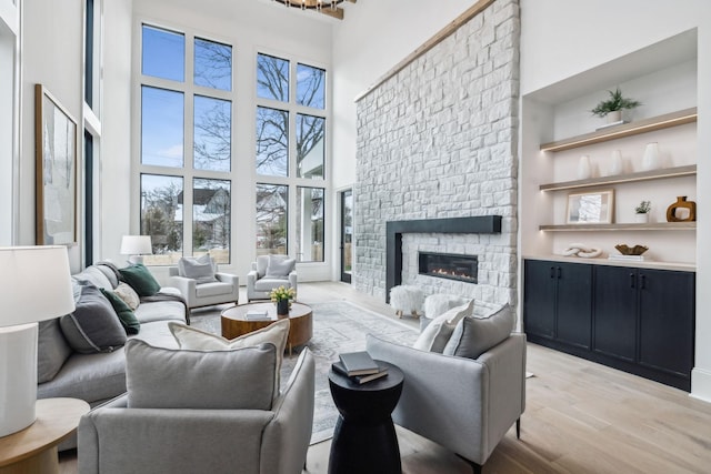 living room featuring light wood-type flooring, a fireplace, and a high ceiling