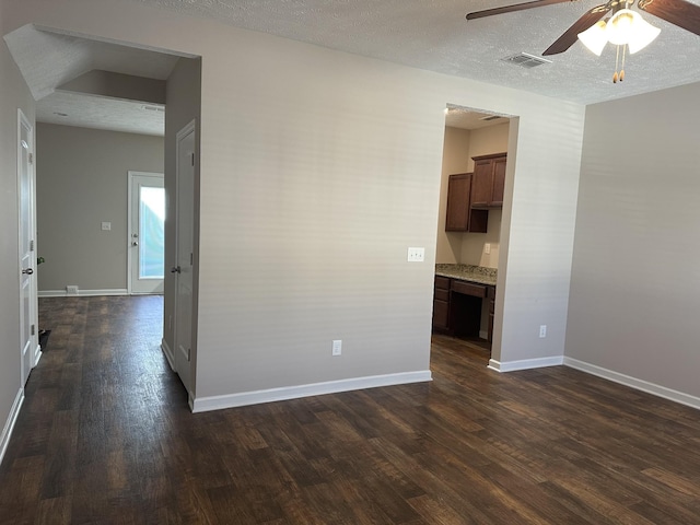 spare room with built in desk, a textured ceiling, ceiling fan, and dark wood-type flooring