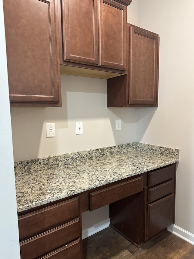 kitchen with built in desk, dark wood-type flooring, and light stone counters