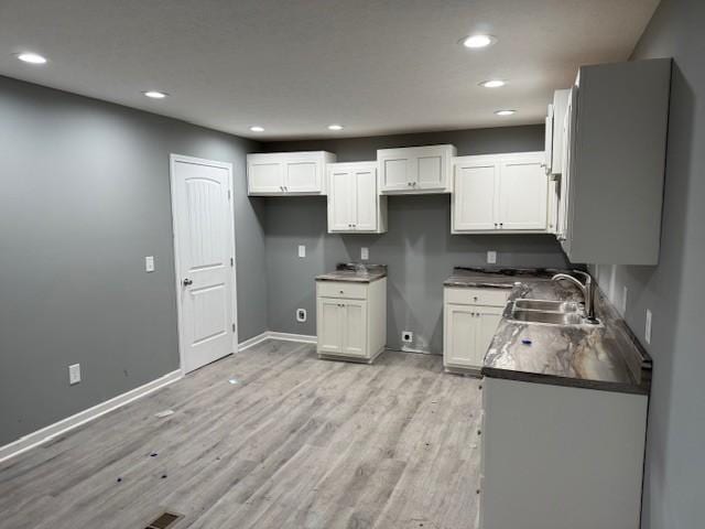 kitchen featuring baseboards, light wood-style flooring, white cabinetry, a sink, and recessed lighting