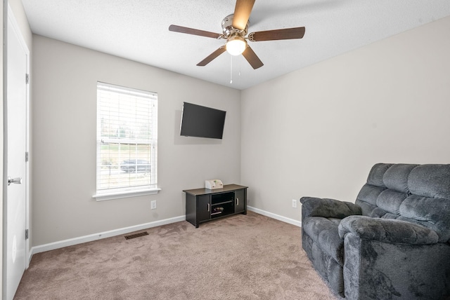 living area with ceiling fan, light colored carpet, and a textured ceiling