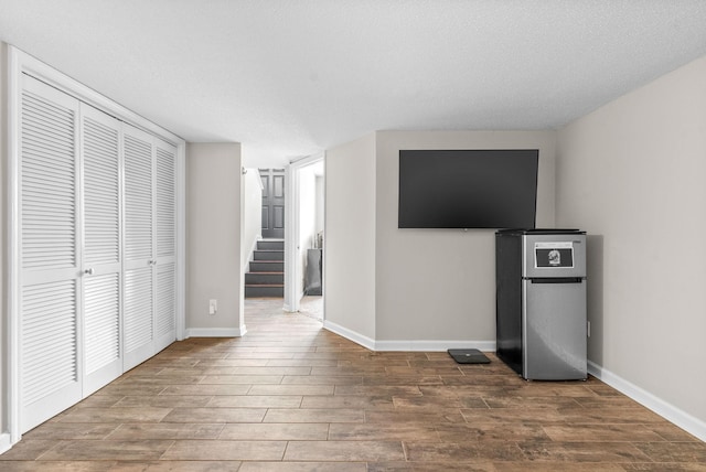 unfurnished bedroom featuring stainless steel fridge, a textured ceiling, a closet, and hardwood / wood-style floors