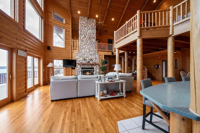 living room with beam ceiling, wooden ceiling, a stone fireplace, high vaulted ceiling, and light wood-type flooring