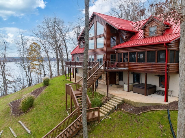 rear view of property with a sunroom, a yard, a deck with water view, a hot tub, and a patio area