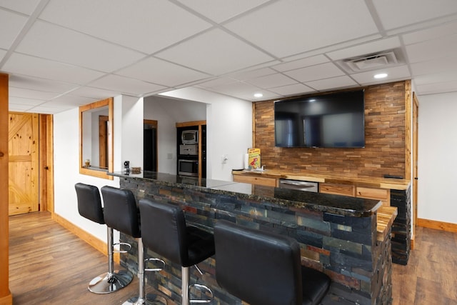 bar with a paneled ceiling, light wood-type flooring, and appliances with stainless steel finishes