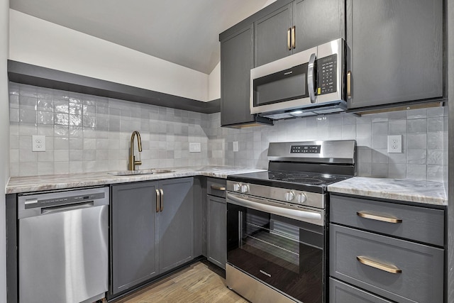 kitchen featuring sink, decorative backsplash, light stone countertops, appliances with stainless steel finishes, and light hardwood / wood-style floors