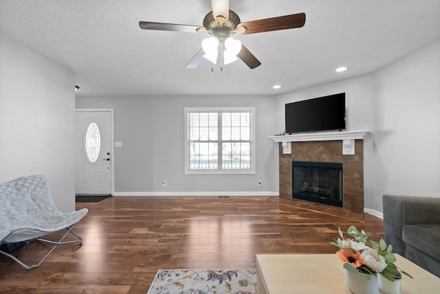 living room with dark hardwood / wood-style flooring, a tiled fireplace, and ceiling fan