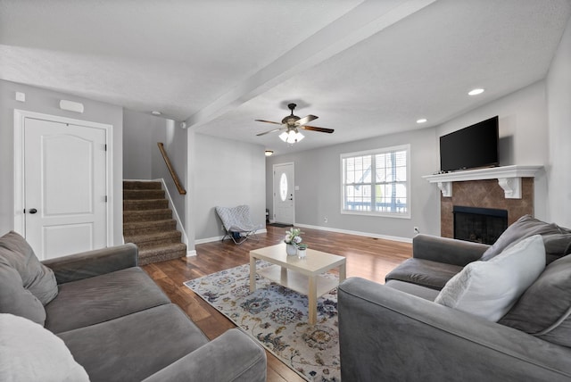 living room with a tile fireplace, dark hardwood / wood-style floors, ceiling fan, and beam ceiling