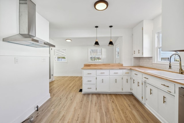 kitchen with white cabinets, a healthy amount of sunlight, decorative light fixtures, and wall chimney exhaust hood