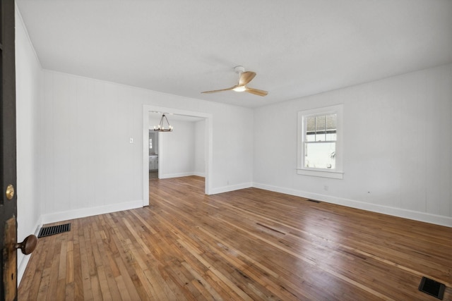 empty room with ceiling fan with notable chandelier and hardwood / wood-style flooring