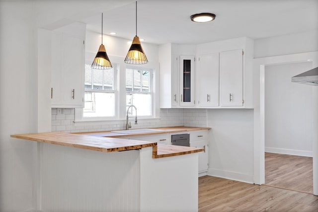 kitchen with pendant lighting, white cabinets, sink, butcher block countertops, and kitchen peninsula