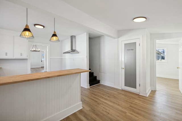 kitchen featuring kitchen peninsula, pendant lighting, light hardwood / wood-style floors, and wall chimney range hood