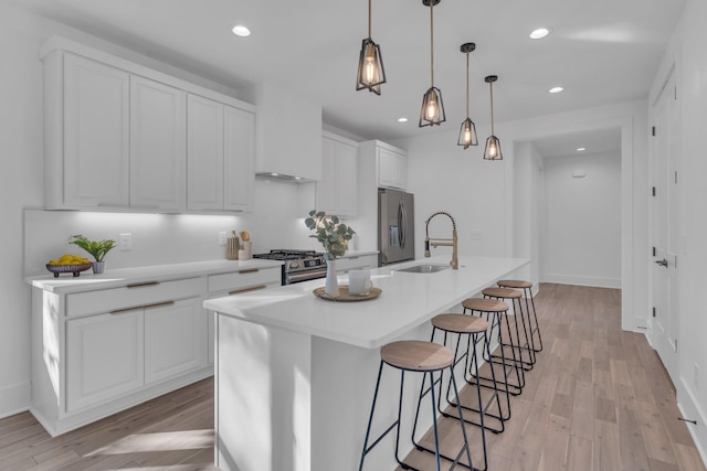 kitchen featuring stainless steel appliances, decorative light fixtures, a center island with sink, white cabinets, and light wood-type flooring