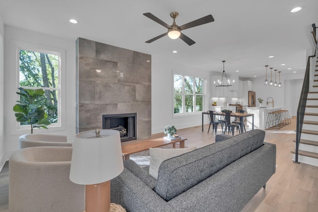 living room with a tiled fireplace, light hardwood / wood-style flooring, ceiling fan with notable chandelier, and sink