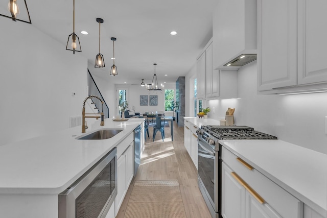 kitchen with sink, stainless steel appliances, premium range hood, light hardwood / wood-style floors, and white cabinets