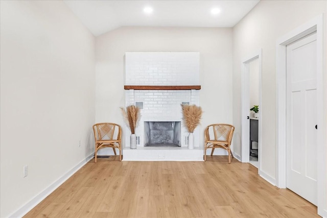 unfurnished room with vaulted ceiling, a brick fireplace, and light hardwood / wood-style floors