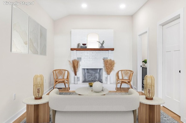 sitting room featuring hardwood / wood-style flooring, a brick fireplace, and lofted ceiling