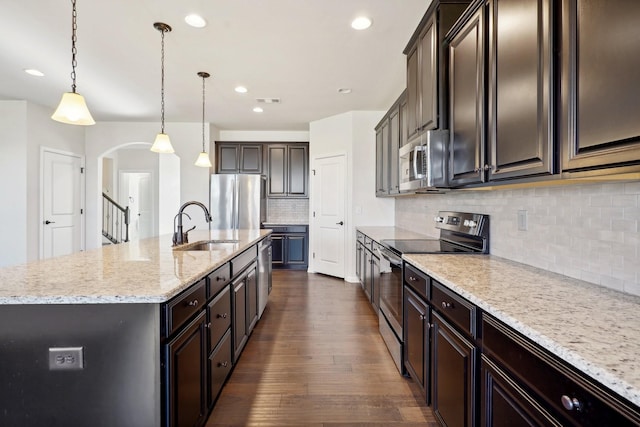 kitchen featuring sink, dark wood-type flooring, stainless steel appliances, an island with sink, and decorative light fixtures