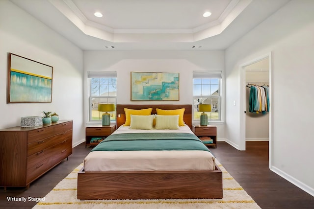 bedroom featuring a tray ceiling, multiple windows, a walk in closet, and dark hardwood / wood-style flooring