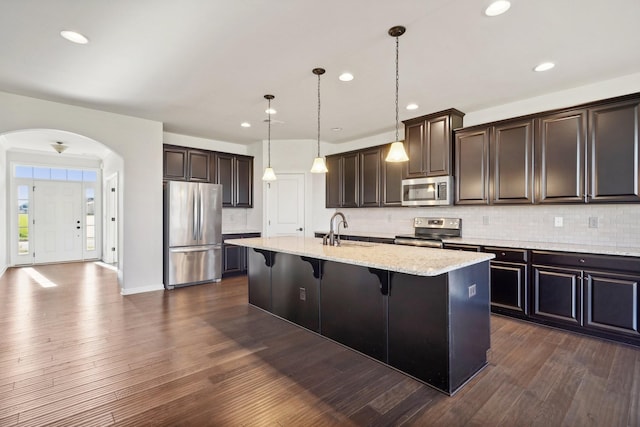 kitchen with sink, an island with sink, dark wood-type flooring, and appliances with stainless steel finishes