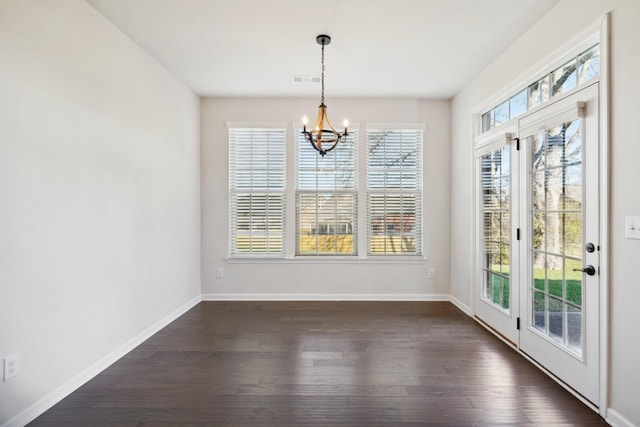 unfurnished dining area with plenty of natural light, dark hardwood / wood-style floors, and an inviting chandelier