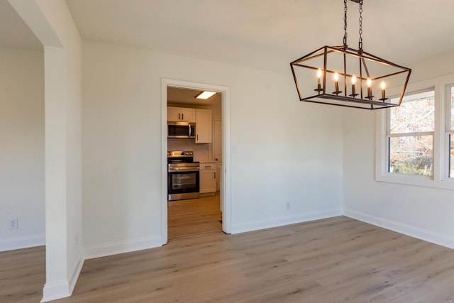 unfurnished dining area featuring a chandelier and light hardwood / wood-style flooring