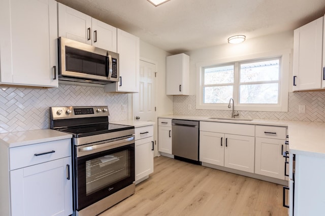 kitchen featuring backsplash, white cabinets, sink, light hardwood / wood-style flooring, and appliances with stainless steel finishes