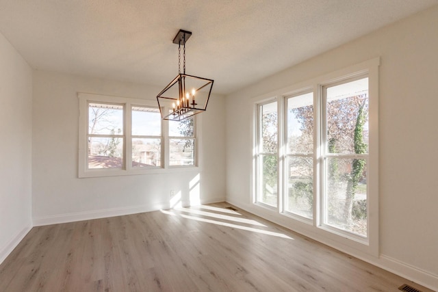 unfurnished dining area with a chandelier, a wealth of natural light, light hardwood / wood-style floors, and a textured ceiling