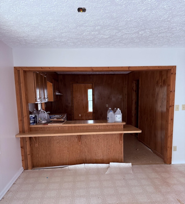 kitchen featuring kitchen peninsula, wooden walls, and a textured ceiling