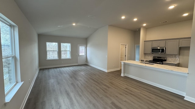 kitchen featuring appliances with stainless steel finishes, lofted ceiling, tasteful backsplash, light stone counters, and gray cabinetry