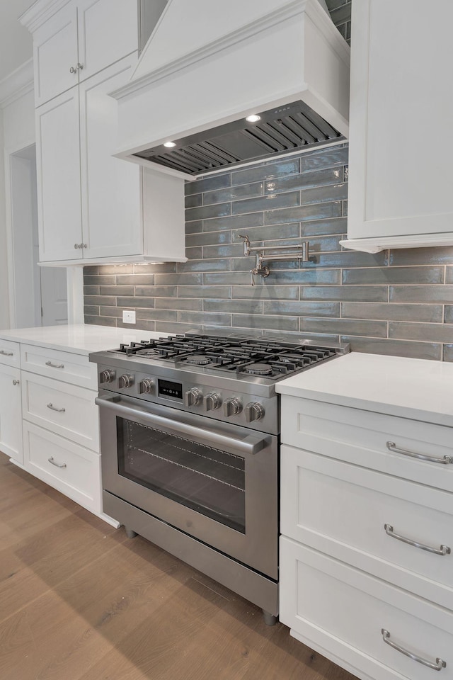 kitchen featuring white cabinets, light countertops, stainless steel range with gas stovetop, and custom range hood