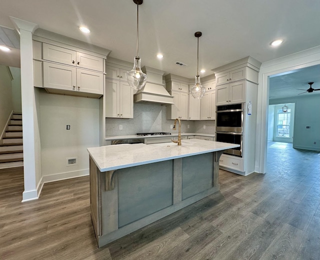 kitchen featuring light stone countertops, appliances with stainless steel finishes, decorative light fixtures, white cabinetry, and an island with sink