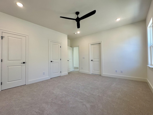 unfurnished bedroom with ceiling fan, recessed lighting, light colored carpet, baseboards, and two closets