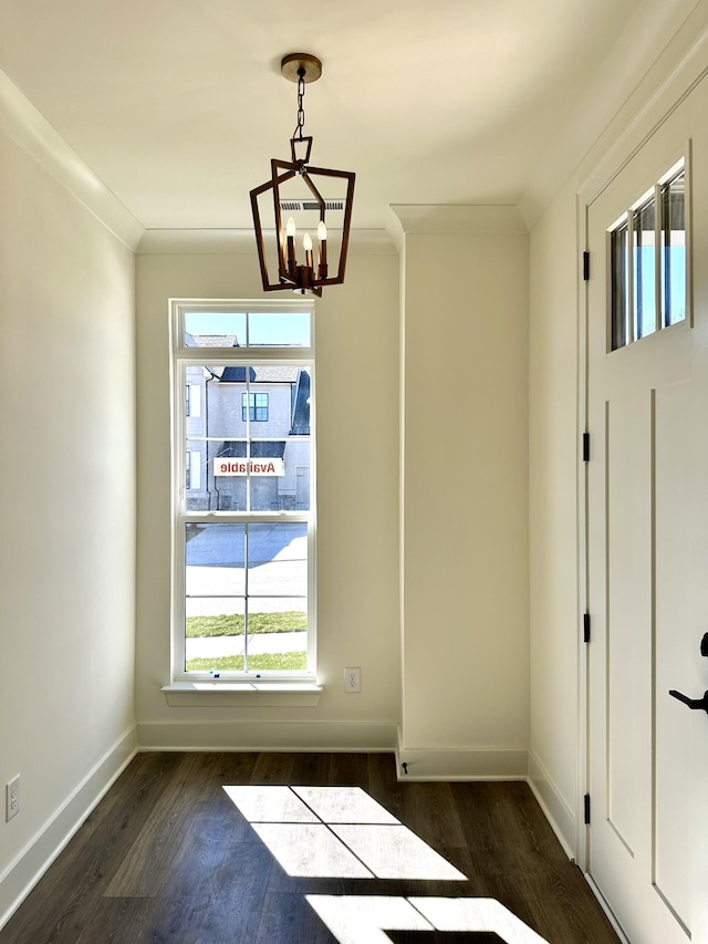 unfurnished dining area featuring dark wood-style floors, baseboards, a chandelier, and crown molding