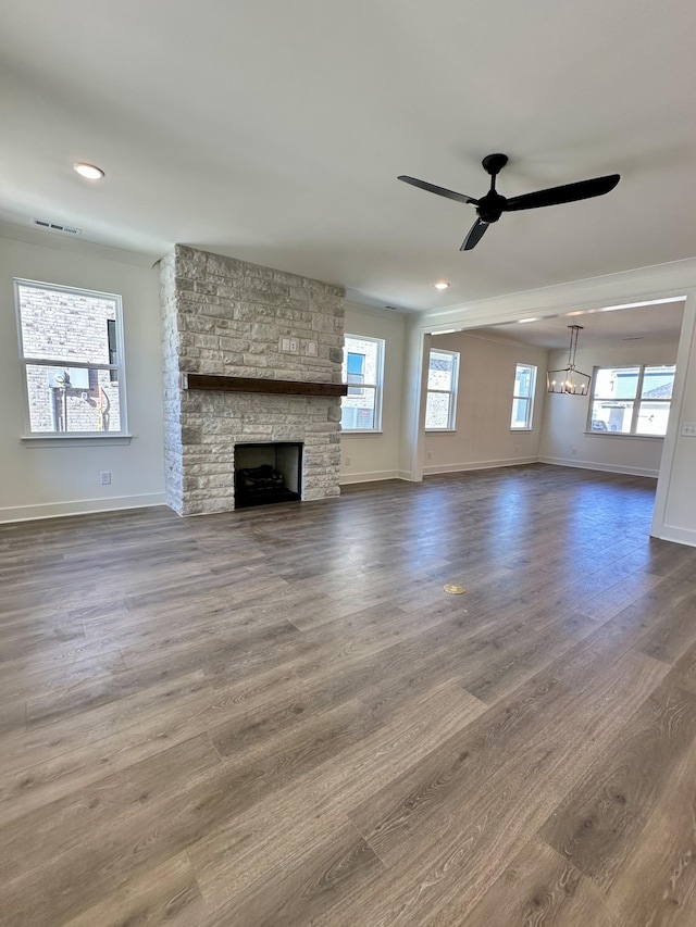 unfurnished living room featuring ceiling fan with notable chandelier, a fireplace, visible vents, baseboards, and dark wood finished floors