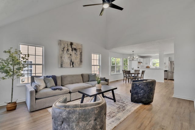 living room with ceiling fan with notable chandelier, light hardwood / wood-style floors, and high vaulted ceiling