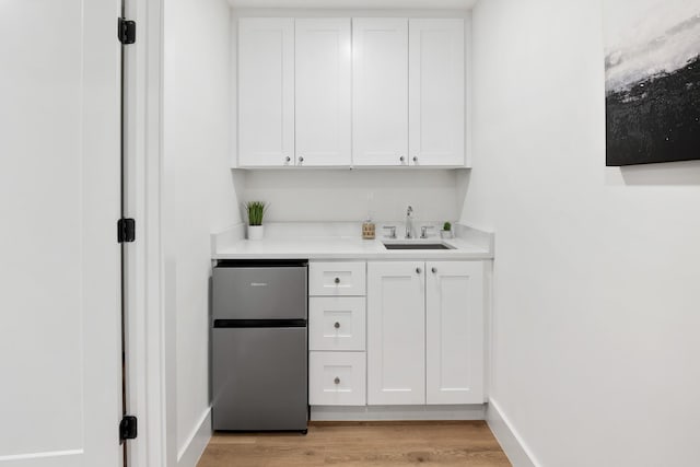 bar with stainless steel fridge, sink, white cabinets, and light hardwood / wood-style flooring