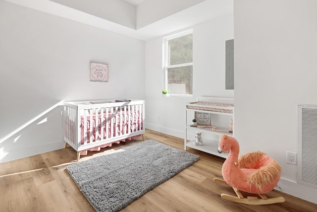 bedroom featuring electric panel, wood-type flooring, and a crib